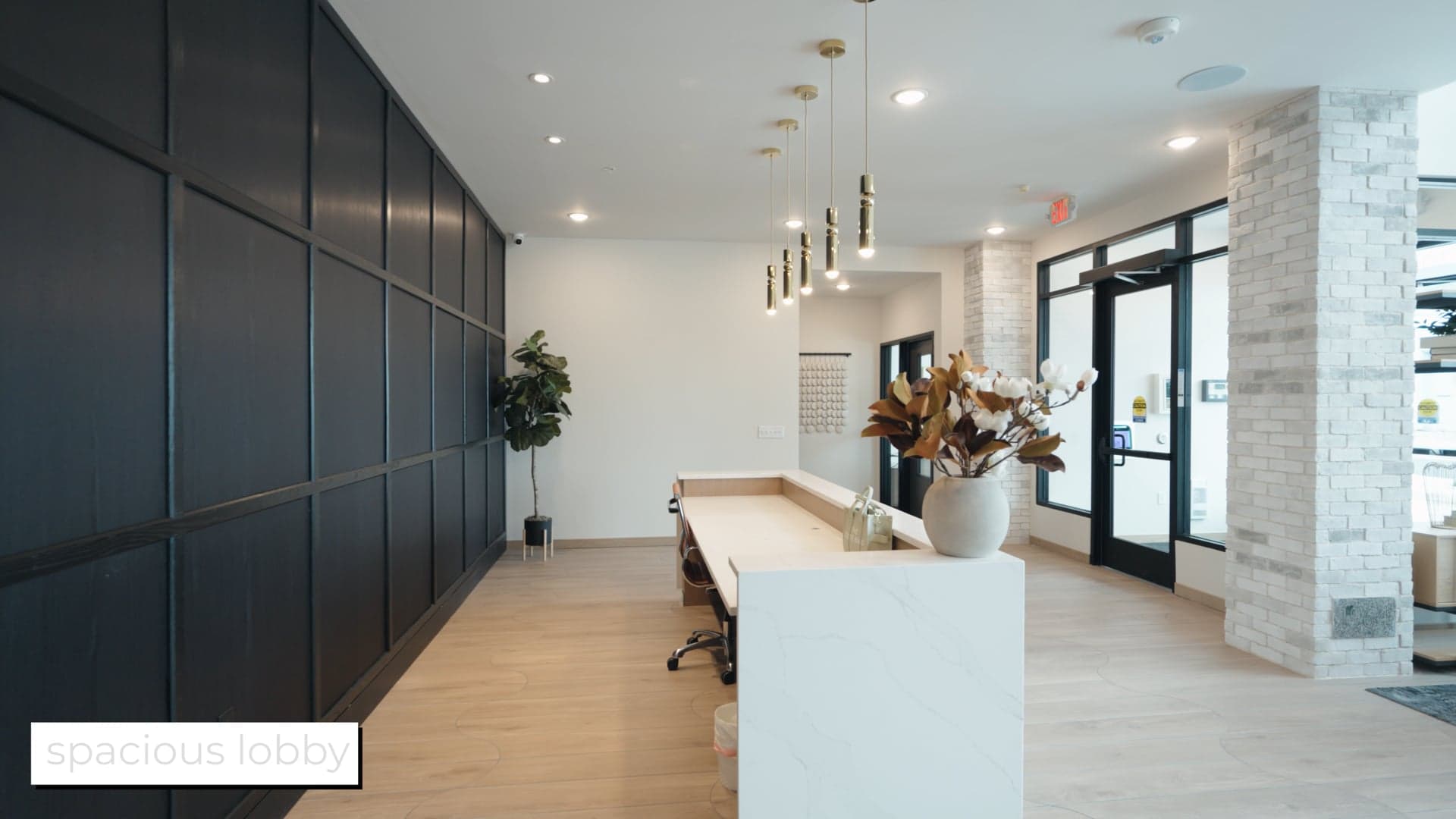 Leasing lobby at First & Banks with black panelled walls, pendant lights and a white desk, on-screen caption reading spacious lobby