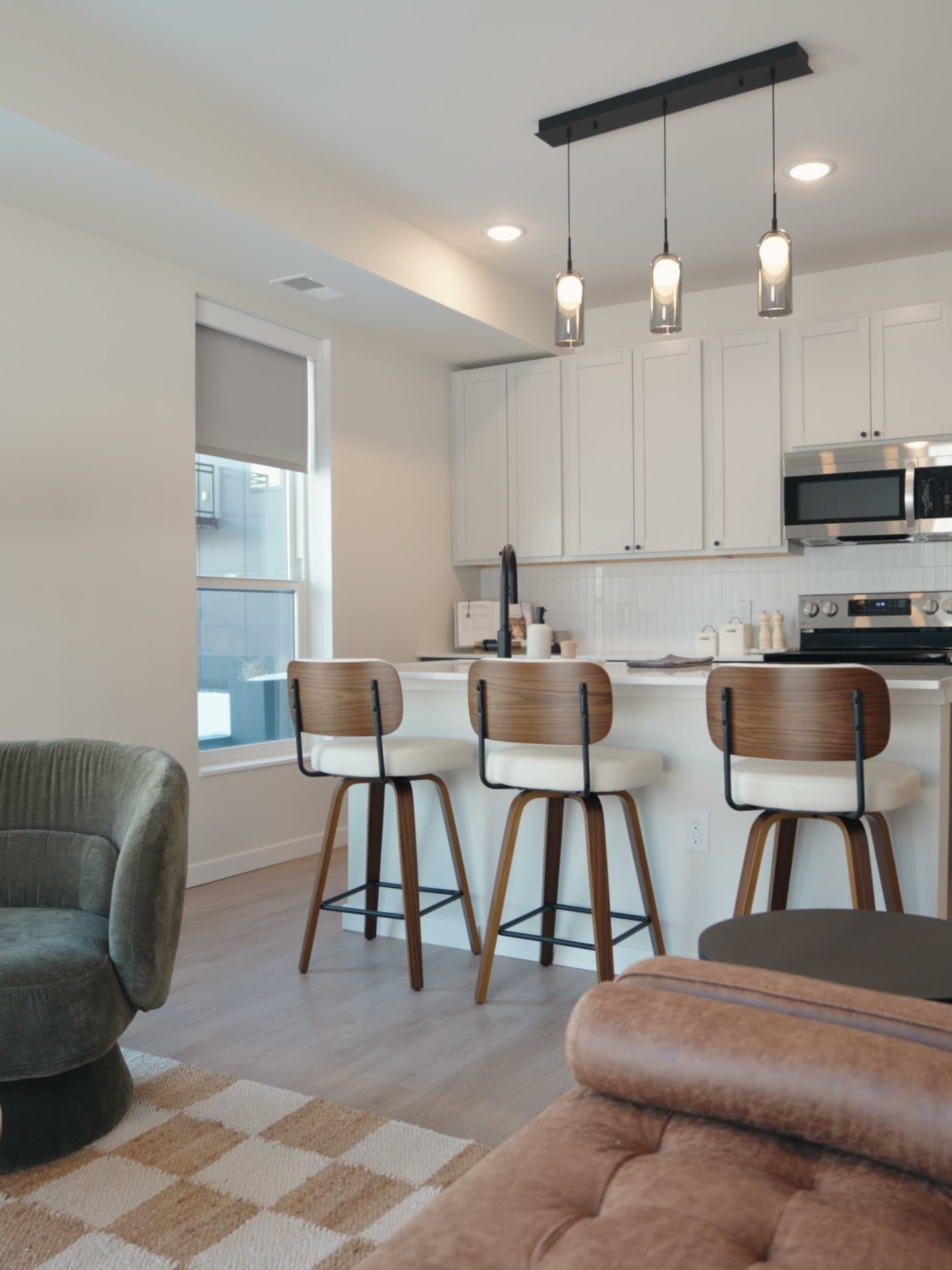 Apartment kitchen at First & Banks with a white island, three stools and pendant lights