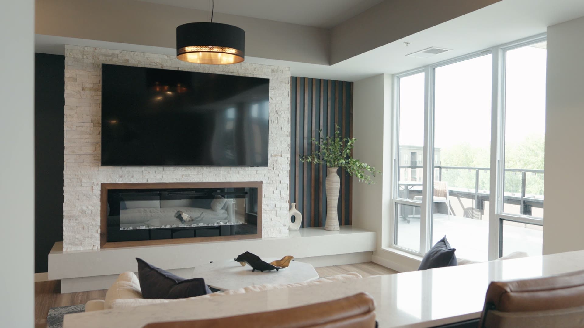 Living room at The Brooks with a mounted TV over a linear fireplace and a wall of balcony glass