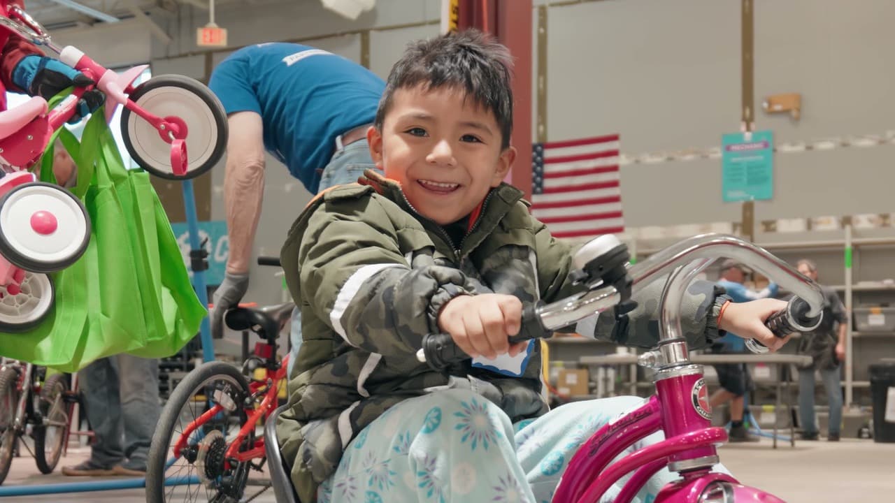 Boy in a camo jacket grinning astride a new bike in the Free Bikes for Kids handout tent