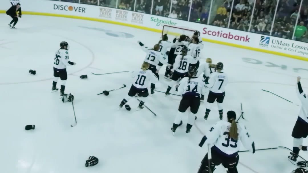 PWHL players piling onto the ice in celebration with gloves and sticks scattered around them