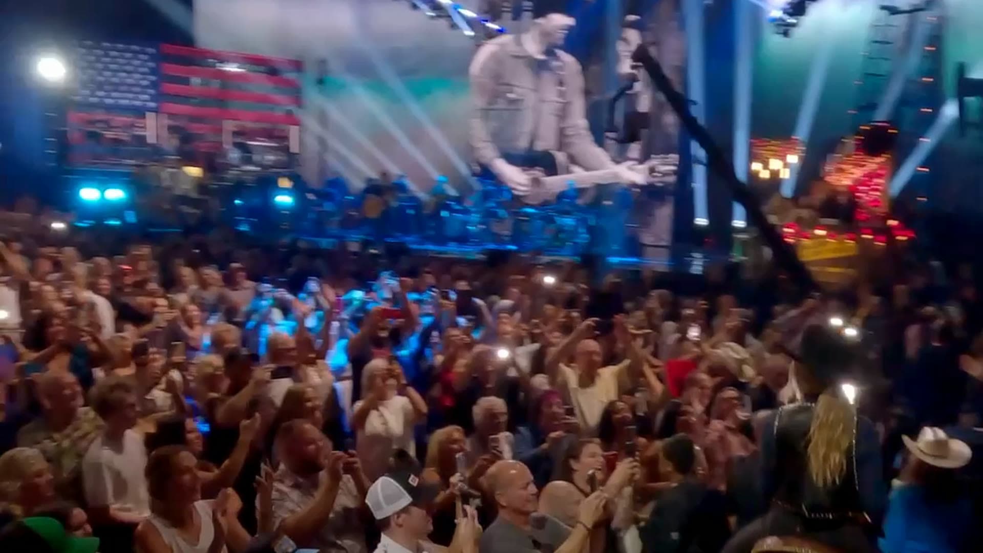 Dense crowd with phones raised in front of a big screen and stage lights at a live event