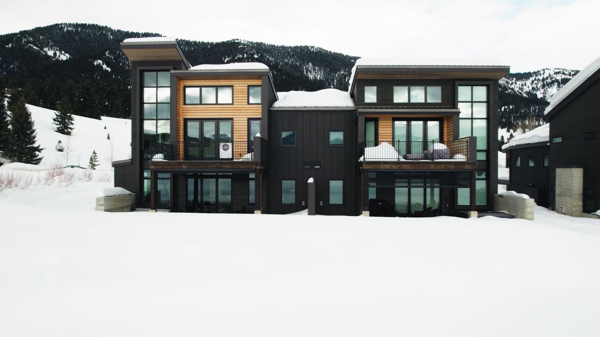 Modern dark-clad home standing in snow at the base of a mountain ridge